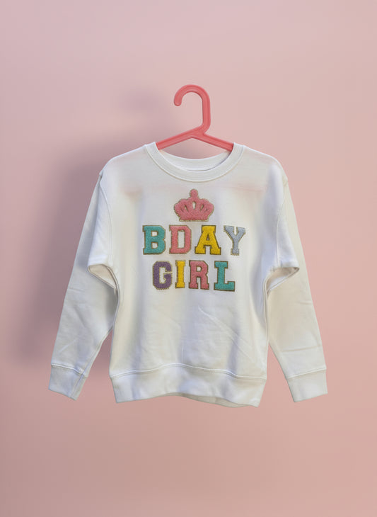 White sweatshirt with colorful 'BDAY GIRL' text and pink crown on a hanger against a light background